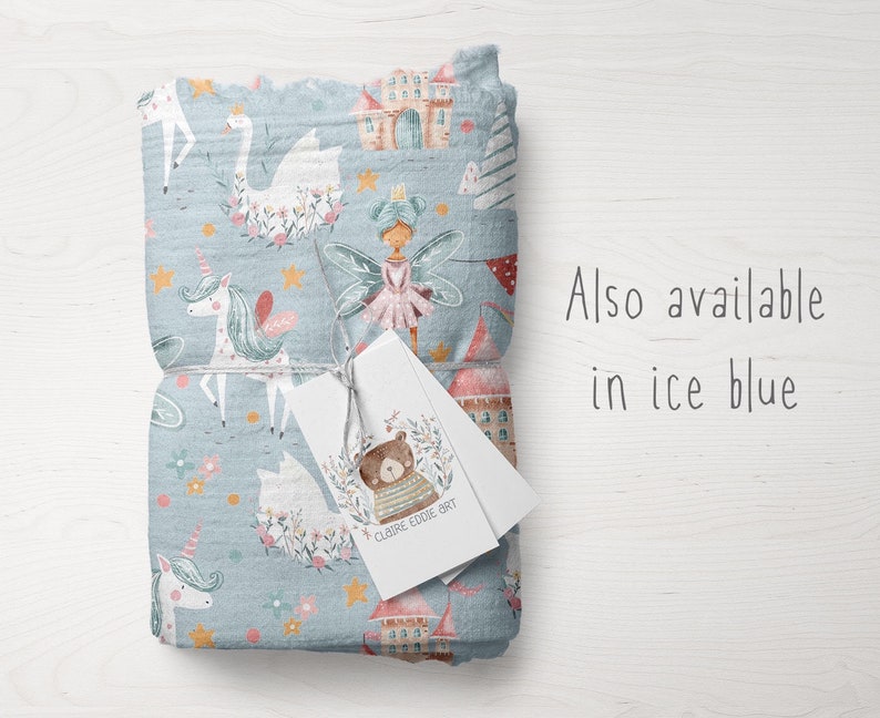May include: A blue fabric with a whimsical pattern featuring unicorns, fairies, swans, stars, and castles. The fabric is folded and tied with a white tag that says "Claire Eddie Art". The text "Also available in ice blue" is written in black on a white background.