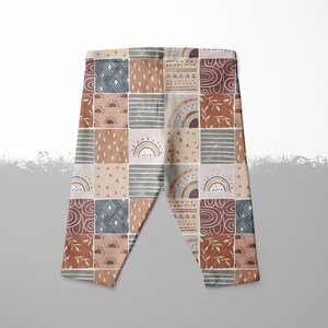May include: A pair of brown, beige, and blue leggings with a patchwork pattern featuring rainbows, suns, and geometric shapes.