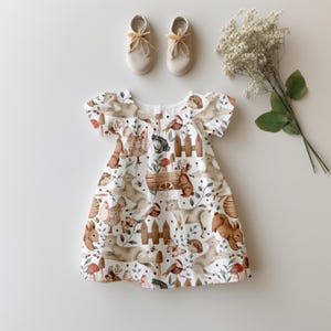 May include: A white dress with a woodland animal print. The dress has short sleeves and a gathered bodice. The print features squirrels, rabbits, birds, and other woodland creatures.