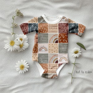 May include: A white baby onesie with a patchwork design featuring geometric shapes, rainbows, and abstract patterns in shades of brown, beige, and rust. The onesie has a short sleeve and a snap closure.