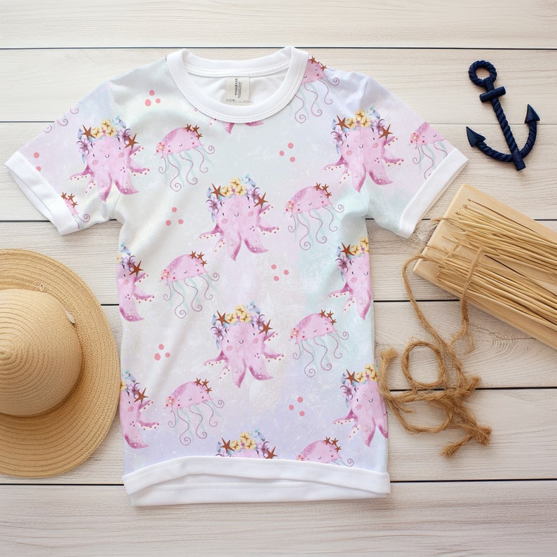May include: White t-shirt with a pink octopus and jellyfish pattern. The octopus is wearing a flower crown and the jellyfish has a blue and white pattern.