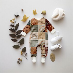 May include: A brown, green, and orange baby onesie with a geometric pattern. The onesie has a zipper down the front and features a rainbow, sun, and geometric shapes.