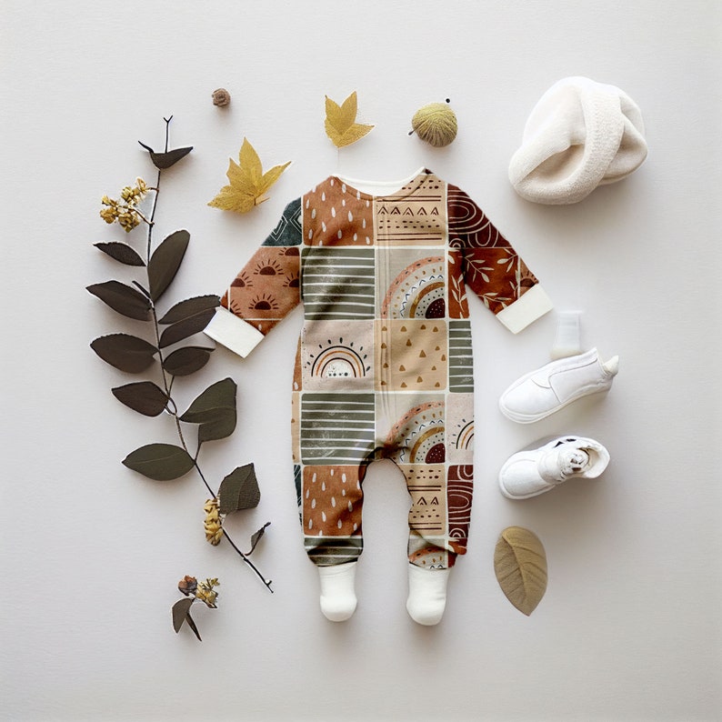 May include: A brown, green, and orange baby onesie with a geometric pattern. The onesie has a zipper down the front and features a rainbow, sun, and geometric shapes.
