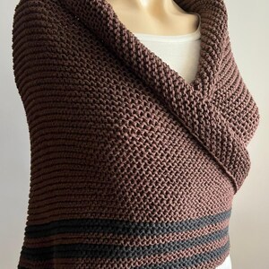 May include: A brown knitted shawl with black stripes at the bottom. The shawl is folded over to create a cowl neck.