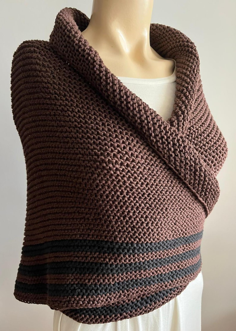 May include: A brown knitted shawl with black stripes at the bottom. The shawl is folded over to create a cowl neck.