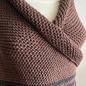 May include: A brown knitted cowl with two black stripes at the bottom. The cowl is folded over and draped around a person's neck.