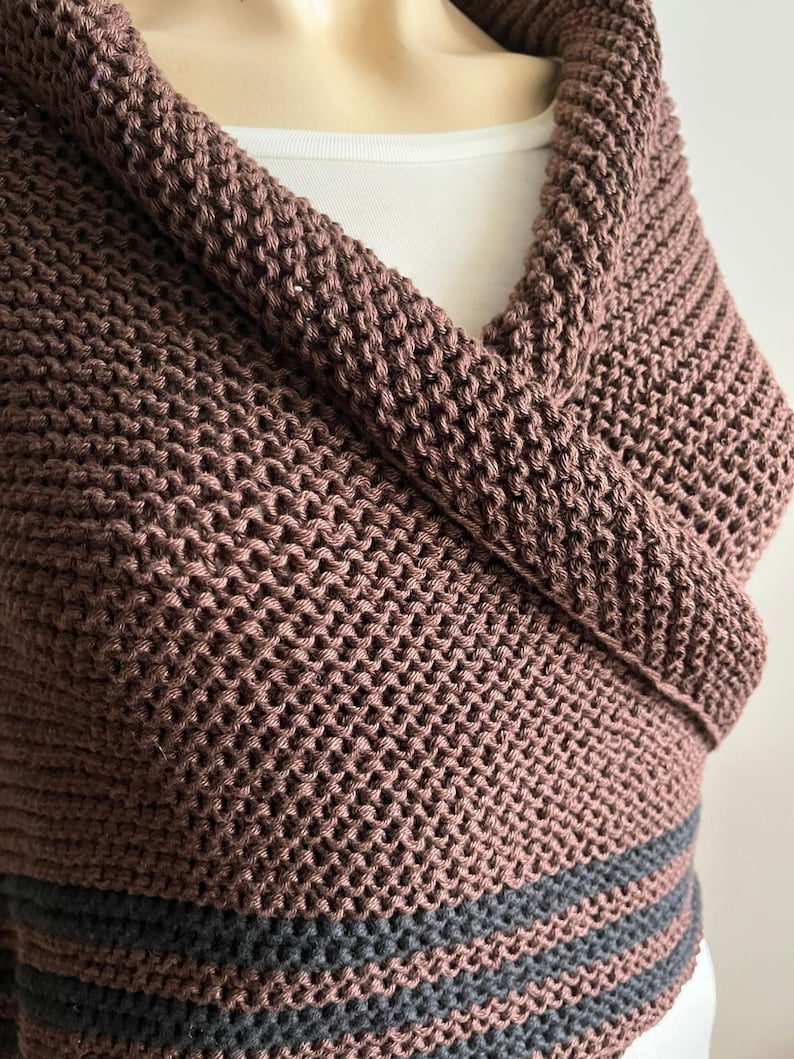 May include: A brown knitted cowl with two black stripes at the bottom. The cowl is folded over and draped around a person's neck.