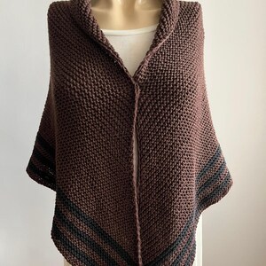 May include: A brown knitted shawl with black stripes along the edges. The shawl is draped over a mannequin.
