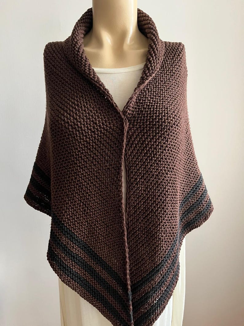 May include: A brown knitted shawl with black stripes along the edges. The shawl is draped over a mannequin.