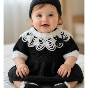 Puede incluir: Un bebé con un vestido negro de ganchillo con cuello y puños blancos, y un gorro a juego. El gorro y el vestido presentan diseños de telarañas. El bebé también lleva botines negros con ribetes blancos. El conjunto está hecho a mano.