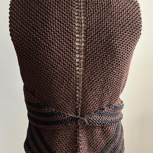 May include: A brown knitted vest with a black trim and a button closure. The vest has a unique open back design.