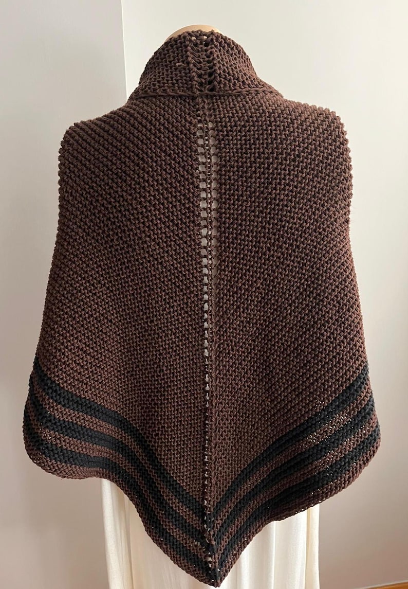 May include: A brown knitted shawl with black stripes along the edges. The shawl is draped over a mannequin.
