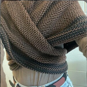 May include: A brown and black knitted scarf with a textured pattern. The scarf is folded and draped over a person's shoulders.