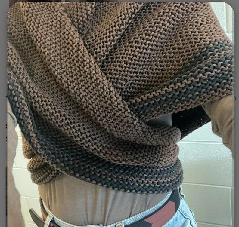 May include: A brown and black knitted scarf with a textured pattern. The scarf is folded and draped over a person's shoulders.