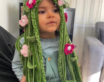 May include: A child wearing a green crocheted hat with pink and white flowers and long green crocheted braids.