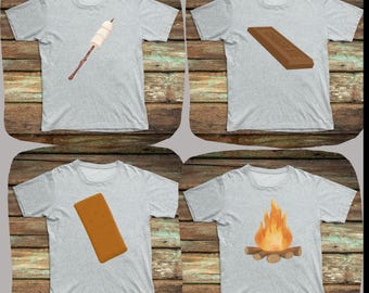 May include: Four gray t-shirts with different images printed on them. The images are a marshmallow on a stick, a chocolate bar, a graham cracker, and a campfire.