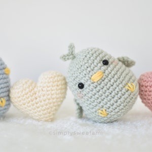 Może przedstawiać: Zestaw dzianych amigurumi ptak&oacute;w z ż&oacute;łtymi dziobami i czarnymi oczami, każdy siedzący obok dzianego serca. Serca są w kolorze kremowym, r&oacute;żowym i jasnoniebieskim.