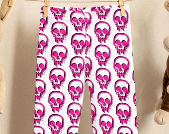 May include: White leggings featuring a repeating pattern of pink skulls. The skulls have a dripping effect and are set against a white background. The leggings are hanging on a clothesline with two soft toys on either side.
