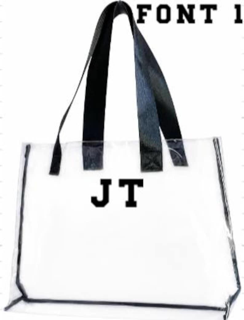 Może przedstawiać: Przezroczysta torba typu tote z czarnymi uchwytami i wykończeniami. Torba posiada inicjały "JT" w pogrubionej, czarnej czcionce. Tekst "FONT 1" jest wydrukowany u g&oacute;ry. Torba jest przeznaczona do przenoszenia przedmiot&oacute;w.