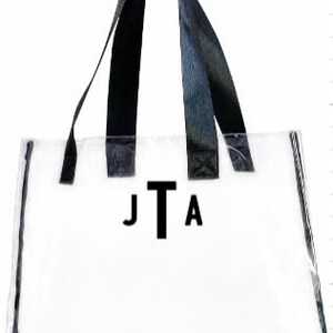 Może przedstawiać: Przezroczysta torba typu tote z czarnymi obramowaniami i uchwytami. Torba posiada monogram "JTA" w czarnych literach. Słowo "Monogram" jest wydrukowane na g&oacute;rze na czarno.