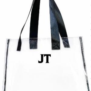 Może przedstawiać: Przezroczysta torba typu tote z czarnymi obramowaniami i uchwytami. Torba zawiera inicjały "JT" w pogrubionych czarnych literach. Tekst "Font 2" jest widoczny w prawym g&oacute;rnym rogu.