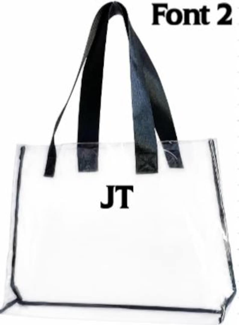 Może przedstawiać: Przezroczysta torba typu tote z czarnymi obramowaniami i uchwytami. Torba zawiera inicjały "JT" w pogrubionych czarnych literach. Tekst "Font 2" jest widoczny w prawym g&oacute;rnym rogu.