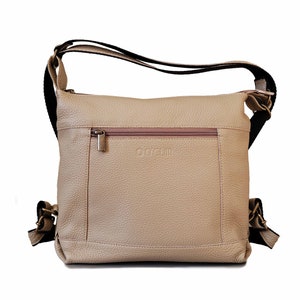May include: A beige leather crossbody bag with a black strap and a zippered pocket on the front. The bag has the word "Oysho" embossed on the front.