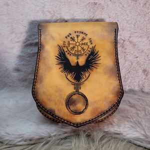 Może przedstawiać: Brązowa skórzana torebka z czarnym kompasem i wzorem kruka. Kompas ma napis "PFYXMR" i "FRM" wokół siebie. Torebka ma klapkę z zatrzaskiem.