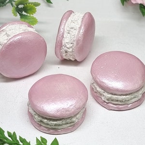 Peut inclure: Quatre macarons roses avec une garniture blanche. Les macarons ont une finition brillante et nacrée.