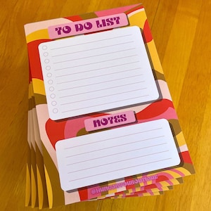 May include: A stack of to-do list and notes pads with a retro 70s design featuring pink, red, yellow, and brown swirls. The top pad has the words "TO DO LIST" and "NOTES" printed on it.