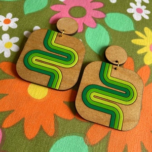 Puede incluir: Pendientes cuadrados de madera con dise&ntilde;o retro. Los pendientes presentan una base de madera marr&oacute;n claro con un dise&ntilde;o ondulado verde, verde lima y verde oscuro. Tienen un peque&ntilde;o perno redondo de madera en la parte superior.