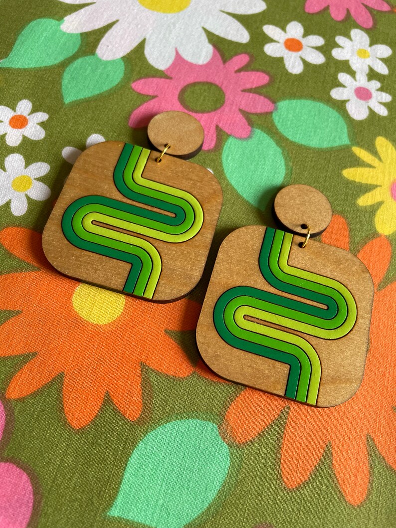 Puede incluir: Pendientes cuadrados de madera con dise&ntilde;o retro. Los pendientes presentan una base de madera marr&oacute;n claro con un dise&ntilde;o ondulado verde, verde lima y verde oscuro. Tienen un peque&ntilde;o perno redondo de madera en la parte superior.