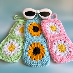 Peut inclure: Trois étuis à lunettes crochetés aux couleurs pastel : vert, bleu et rose. Chaque étui présente un motif floral, avec des pétales blancs et des centres jaunes. Des lunettes de soleil blanches reposent au-dessus des étuis, créant une esthétique estivale et ludique.