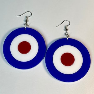 Pode incluir: Um par de brincos redondos em forma de alvo, nas cores azul, branco e vermelho. Os brincos têm um gancho prateado.