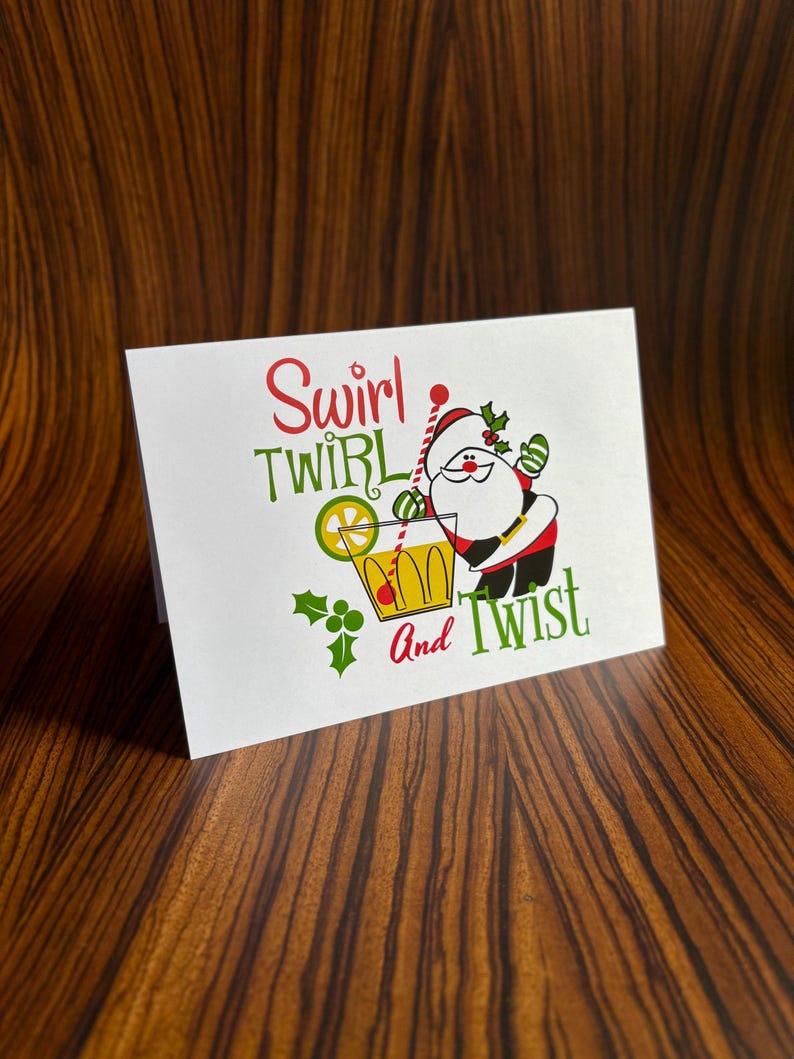 May include: A white card with a red and green illustration of Santa Claus holding a glass of a yellow drink with a lime wedge. The text on the card reads "Swirl Twirl and Twist".