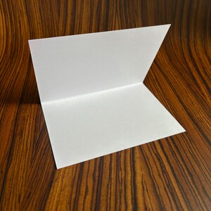 May include: A blank white card folded in half, sitting on a brown wood surface.