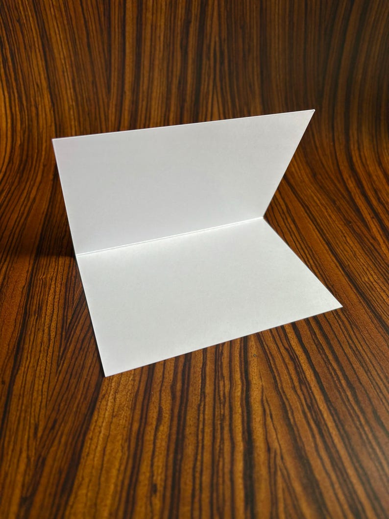 May include: A blank white card folded in half, sitting on a brown wood surface.