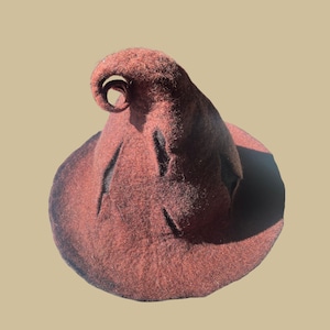 Könnte beinhalten: Ein weinroter Hexenhut mit breiter Krempe und hoher, spitzer Krone. Der Hut hat eine eingerollte Spitze und mehrere dekorative Schlitze. Der Hut besteht aus einem filzartigen Material und ist vor einem neutralen Hintergrund platziert.