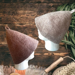 Puede incluir: Dos gorros de sauna c&oacute;nicos hechos de lana fieltrada, uno en tono beige claro y el otro en un tono marr&oacute;n rojizo m&aacute;s oscuro. Cada gorro presenta un peque&ntilde;o lazo en la parte superior puntiaguda y se muestra sobre un maniqu&iacute; blanco.