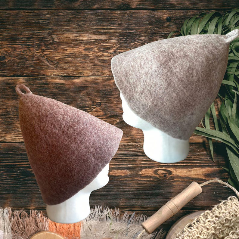 Puede incluir: Dos gorros de sauna c&oacute;nicos hechos de lana fieltrada, uno en tono beige claro y el otro en un tono marr&oacute;n rojizo m&aacute;s oscuro. Cada gorro presenta un peque&ntilde;o lazo en la parte superior puntiaguda y se muestra sobre un maniqu&iacute; blanco.