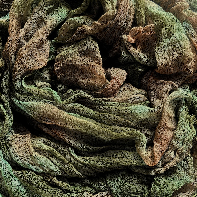 May include: Close-up of a textured fabric with a layered, draped appearance. The fabric features a blend of earthy tones, including shades of brown, green, and hints of teal. The material appears to be lightweight and airy, with visible woven details.