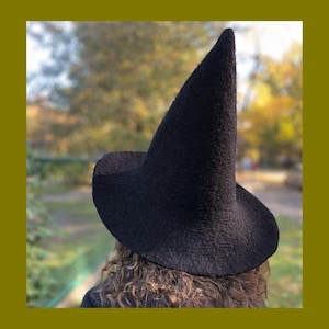 May include: A tall, pointed black hat with a wide, slightly curved brim. The hat features a textured, felted surface and a conical crown that tapers to a rounded tip. The design is solid black throughout, with a structured yet soft appearance.