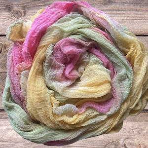 Op de afbeelding: Een veelkleurige stof in roze, gele en groene tinten. Het materiaal heeft een gekreukte textuur, waardoor het een zachte, vloeiende uitstraling heeft. De kleuren vloeien in elkaar over, waardoor een gradiënteffect ontstaat. De stof wordt waarschijnlijk gebruikt voor knutselen of decoratie.