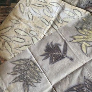 May include: Close-up of several pieces of fabric with leaf imprints. The fabrics are various shades of beige and brown, with the leaf patterns in darker tones. The leaves are of different shapes and sizes, creating a natural, organic aesthetic.