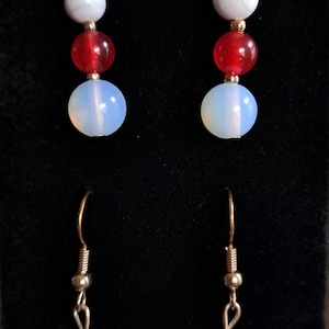 May include: A pair of earrings with three beads each. The top bead is white, the middle bead is red, and the bottom bead is a light blue opal.