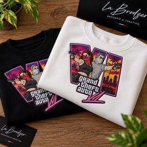 May include: A black and a white sweatshirt, each featuring an embroidered graphic of two characters holding handguns, with palm trees, a city skyline, and the text Grand Theft Auto VI in a purple and pink color palette.