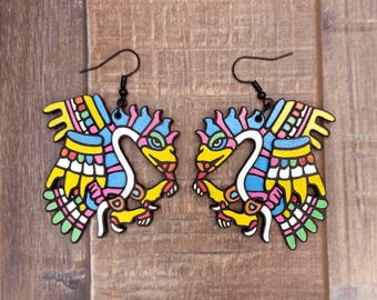 May include: A pair of colorful wooden earrings shaped like mythical creatures with intricate details. The earrings are painted in shades of yellow, blue, pink, green, and white.