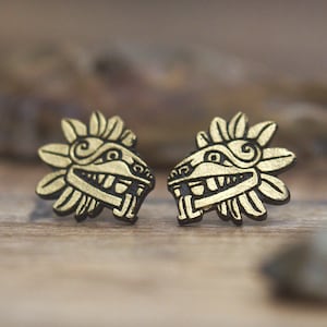May include: A pair of gold-colored earrings with a black outline of a mythical creature with a feathered headdress.