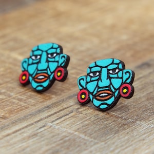 May include: A pair of turquoise blue wooden earrings with red and yellow accents. Each earring features a stylized face with closed eyes and a small mouth.