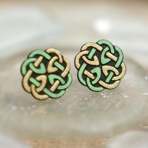 May include: A pair of wooden earrings with a Celtic knot design. The earrings are painted in shades of green and gold.